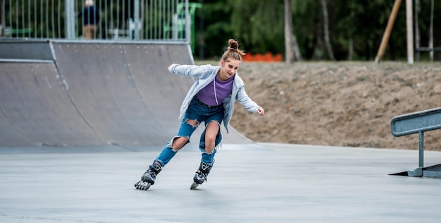 Beautiful girl roller skater riding in city park with ramp pretty female teenager rollerskating in