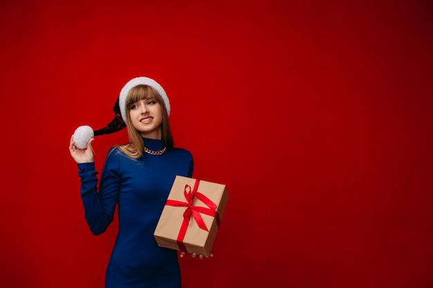 A beautiful girl in a Santa hat holds a New Years gift in her hands on a red background