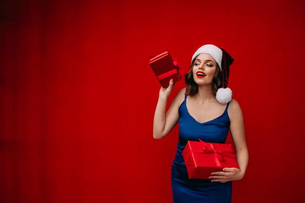 A beautiful girl in a Santa hat holds a New Years gift in her hands on a red background