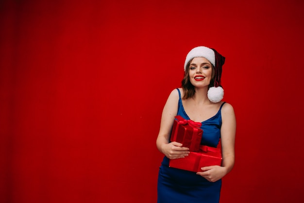 A beautiful girl in a Santa hat holds a New Years gift in her hands on a red background