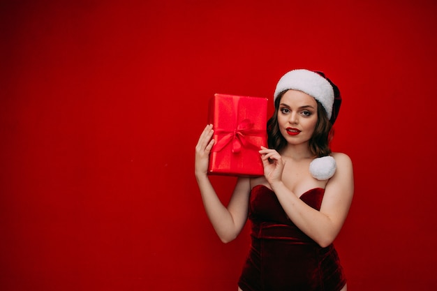 A beautiful girl in a Santa hat holds a New Years gift in her hands on a red background