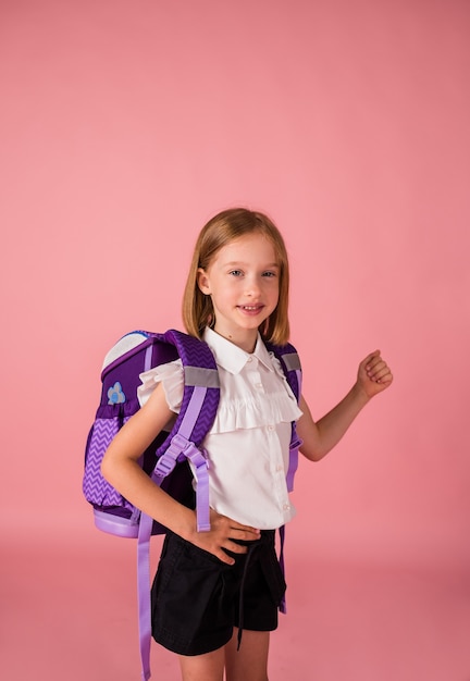 Beautiful girl in a school uniform with a backpack on a pink background with a place for text