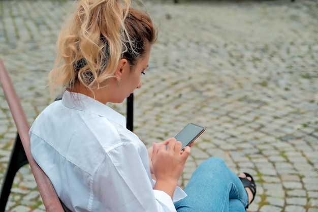 A beautiful girl sits on a bench and holds a phone in her hands the girl orders food through the phone the girl is talking on the phone laughing happy surprised