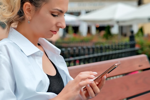 A beautiful girl sits on a bench and holds a phone in her hands the girl orders food through the phone the girl is talking on the phone laughing happy surprised