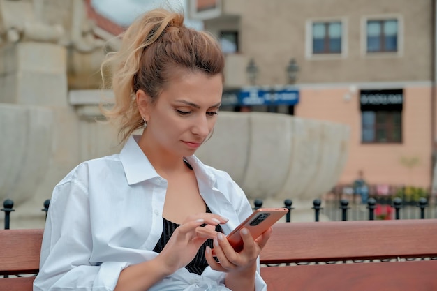 a beautiful girl sits on a bench and holds a phone in her hands. the girl orders food through