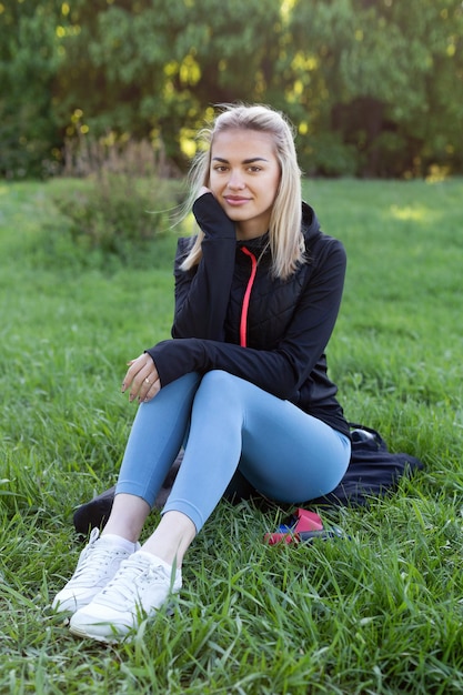 A beautiful girl sits on the grass after a workout Cute model in sportswear in the park