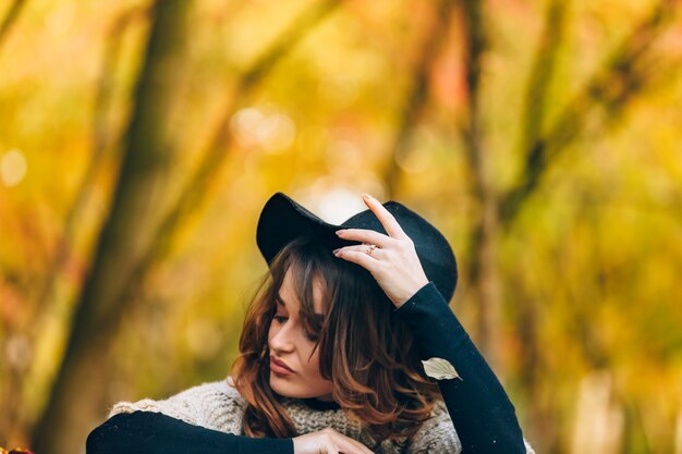 Beautiful girl sits in a park and smoothes her hat