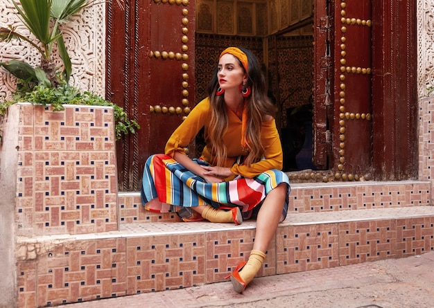 A beautiful girl sits on the stairs near a large wooden door on Essaouira street Morocco