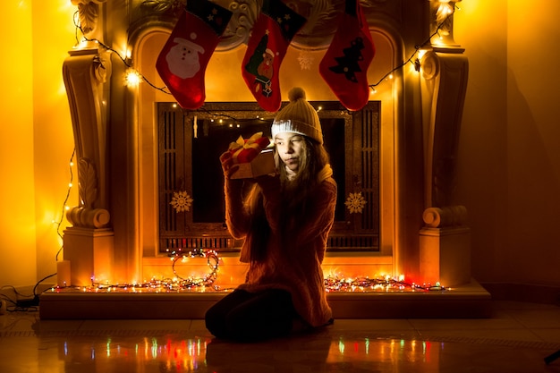 Beautiful girl sitting at dark living room at Christmas and looking inside gift box