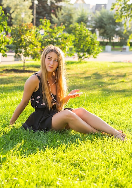 Beautiful girl sitting on the grass in the park and listen to music.