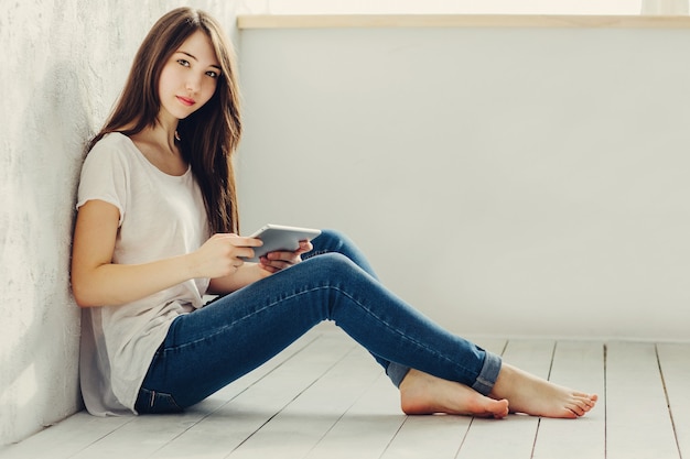 Beautiful girl sitting near the wall and looks in Tablet