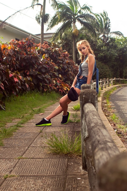 Beautiful girl sitting on a railing on a background of palm trees