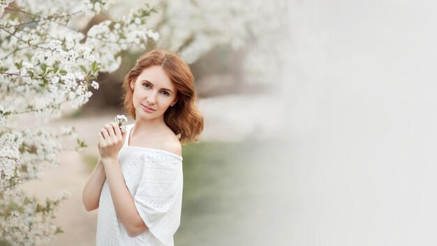 Beautiful girl in the spring next to a blossoming cherry branch Banner with place for text