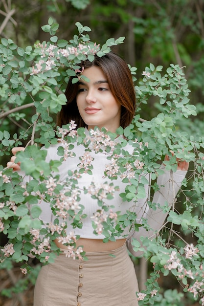 Beautiful girl standing in blooming park holding tree branch looking aside smiling