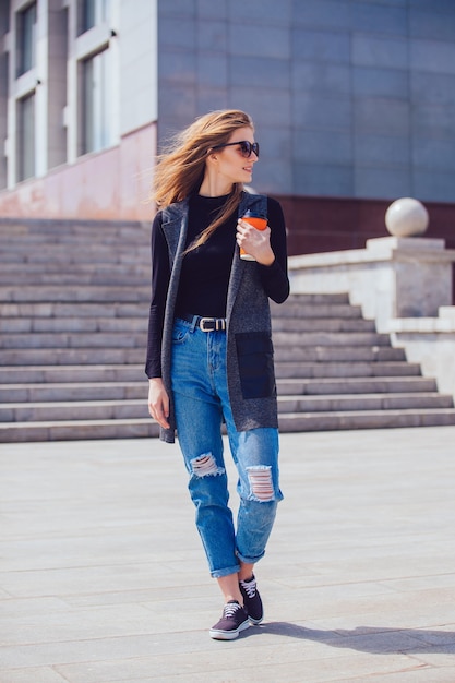 Beautiful girl standing on the street with coffee and glasses.