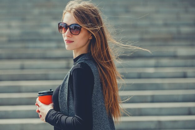 Beautiful girl standing on the street with coffee and glasses.