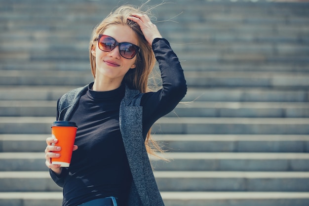 Beautiful girl standing on the street with coffee and glasses.