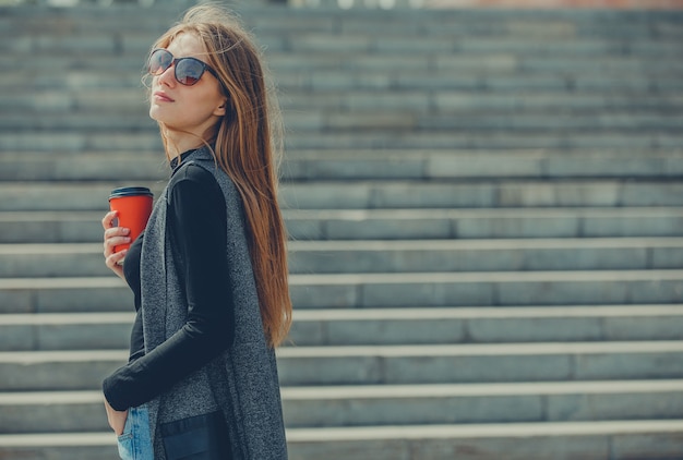 Beautiful girl standing on the street with coffee and glasses.