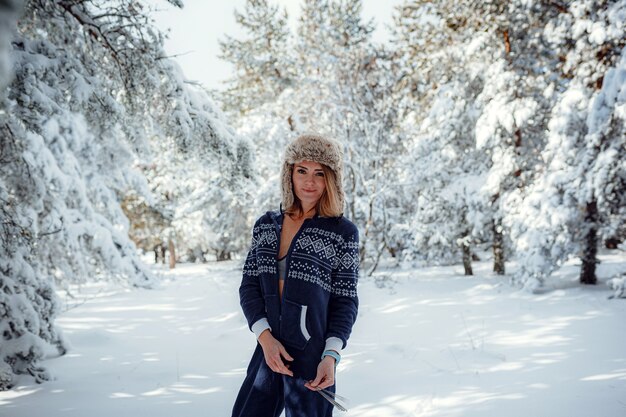 Beautiful girl standing, in winter in forest park, background of Christmas tree snow, she is resting in resort. Free space for text. Blue jumpsuit for sports.