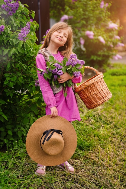 Beautiful girl in straw hat in lilac Garden Girl with lilac flowers in springtime Gardening