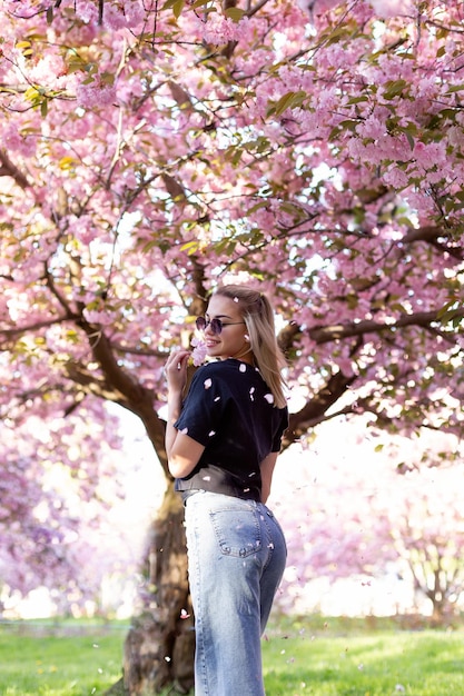 Beautiful girl in sunglasses on the background of flowering sakura trees