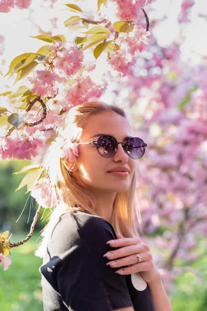 Beautiful girl in sunglasses on the background of flowering sakura trees