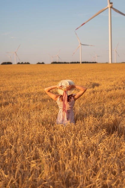 Beautiful girl at sunset in a wheat field with windmills to generate electricity The concept of renewable energy love for nature electricity Renewable energy