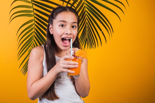 Beautiful girl surprised with a glass of orange juice on a yellow background.