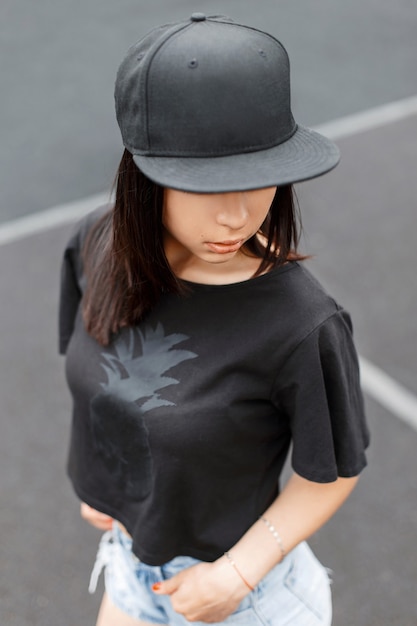 Beautiful girl in swag -style black T-shirt and a cap at the stadium.