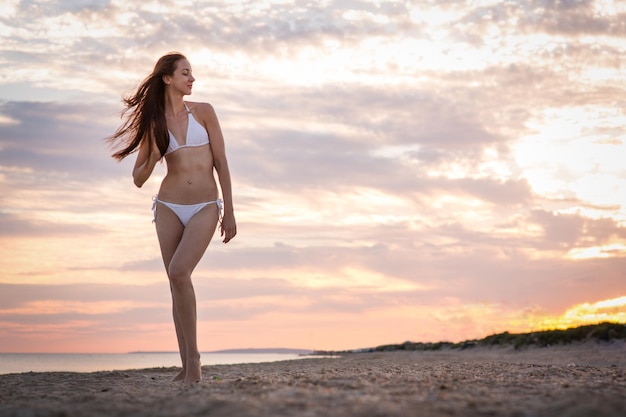 Beautiful girl in a swimsuit on the beach at sunset