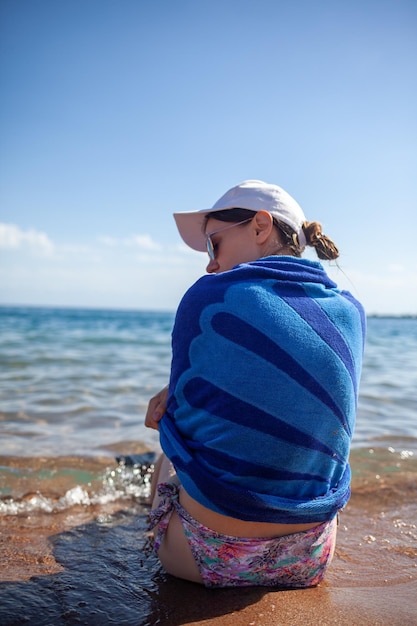 A beautiful girl in a swimsuit with long hair and a white cap looks at the blue sea. Rear view.