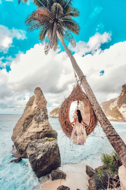 Beautiful girl on swing coconut palms on beach at Daimond beach, Nusa Penida island Bali ,Indonesia