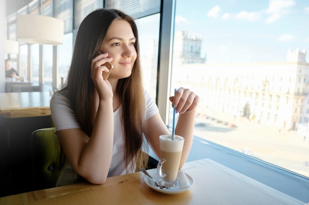 Beautiful girl talking in a cafe on the phone with latte