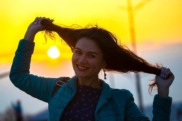 Beautiful girl touches her red hair on the background of the setting sun