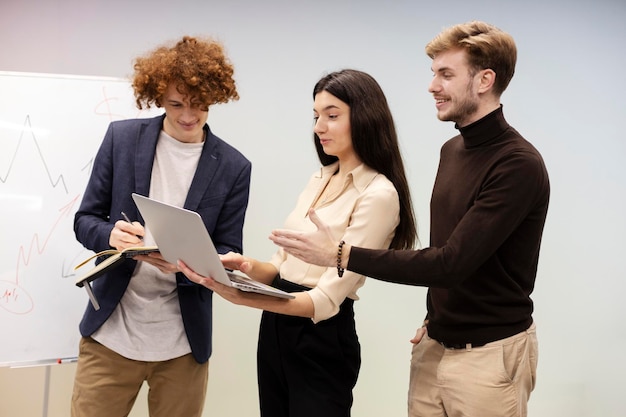 Beautiful girl using laptop standing in modern office her male coworkers standing next to her