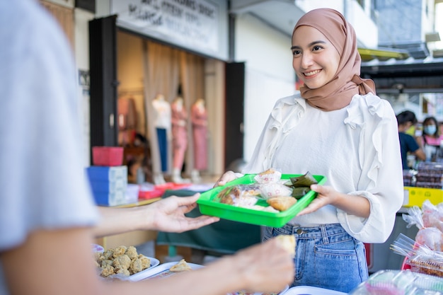 A beautiful girl in a veil give a plastic tray of food eaten upon breaking the fast to seller