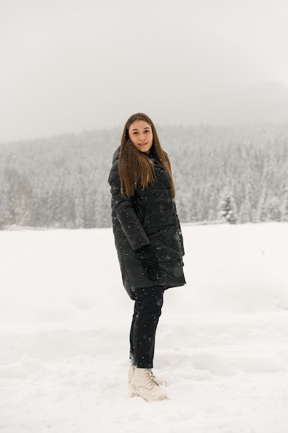 Beautiful girl walking in a snowfall. Young woman in black puffer jacket posing in the winter forest.Outdoor portrait of pretty brunette lady. Winter concept