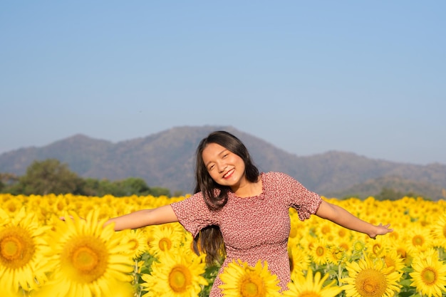 Beautiful girl wear red dress at sunflower field and mountain in the morning