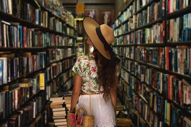 Beautiful girl wearing stylish outfit looking for interesting book in the small vintage bookstore