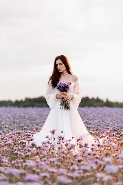 A beautiful girl in a white dress in a blooming field of Provence in a romantic atmosphere with a bouquet in her hands