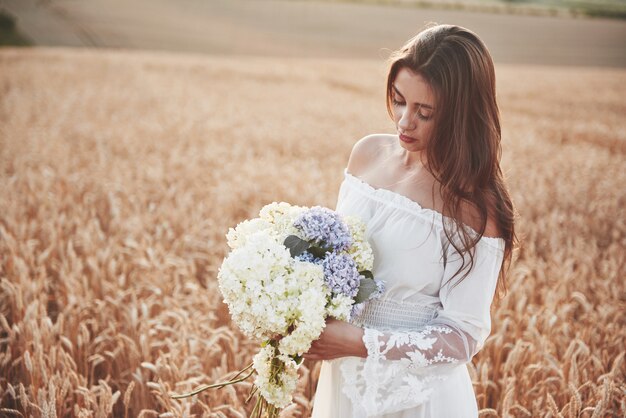 Beautiful girl in white dress running on the autumn field of wheat at sunset time.