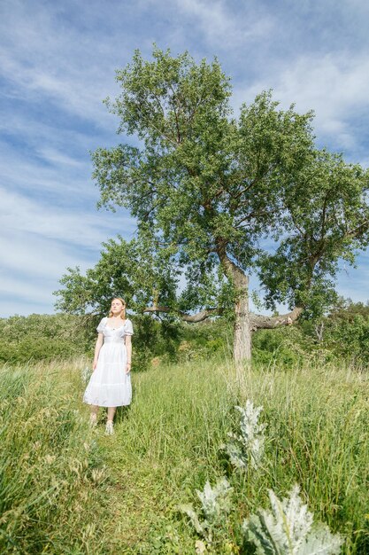 Beautiful girl in a white dress with flowers in a field overlooking the sky