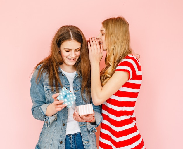 Photo a beautiful girl who makes a gift to her girlfriend and both are happy on a pink background