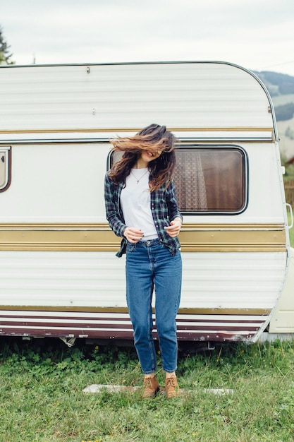 Beautiful girl with backpack traveling Girl standing near trailer traveling in mountains Woman in glasses traveling by car Traveler Girl thumbs up