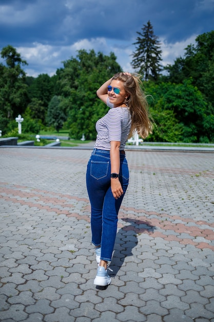 A beautiful girl with blond long hair of European appearance. Dressed in jeans and a T-shirt. Walk on a sunny day