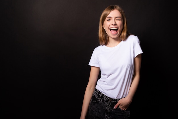 Beautiful girl with happy smile playfully winks. Isolated on black wall