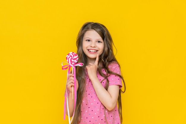 A beautiful girl with a lollipop in her hands holding a large caramel candy with a bow a girl in a very cute pink dress with a lollipop on a stick on an isolated background