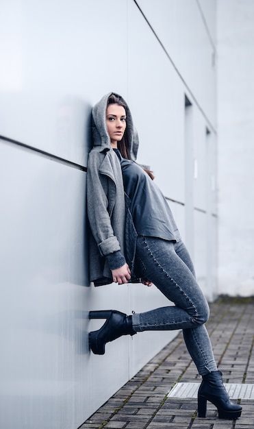 Beautiful girl with long dark hair in a gray sweatshirt and heels on white wall background