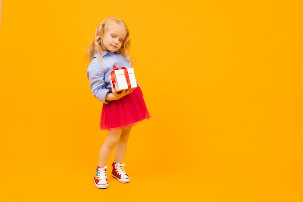 Beautiful girl with long hair smiles and holds a gift, picture isolated on yellow background