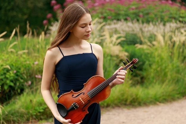 A beautiful girl with long violinists stands in the park in the summer. High quality photo